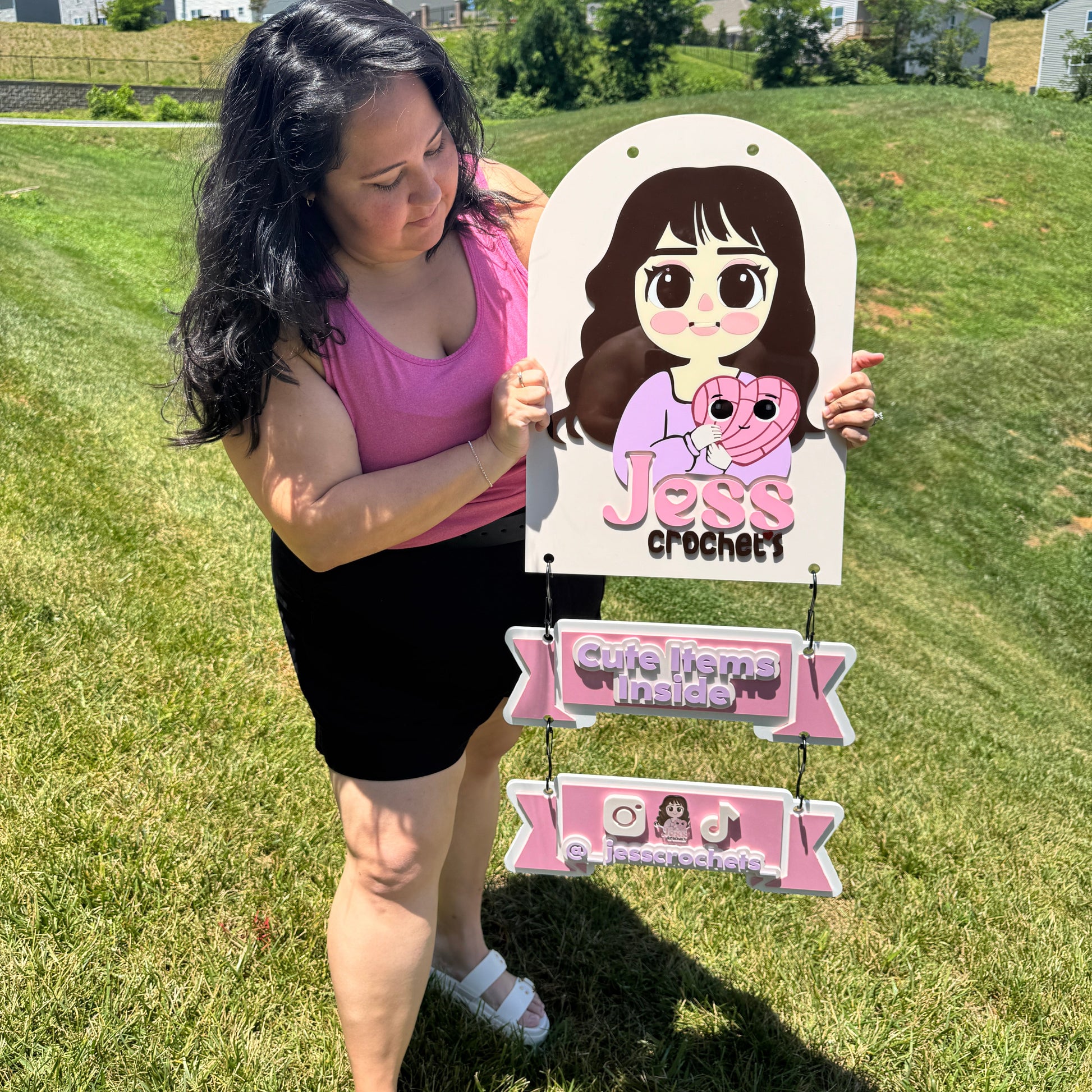 Person holding a cartoon cutout and signs outdoors on a grassy area with houses in the background.