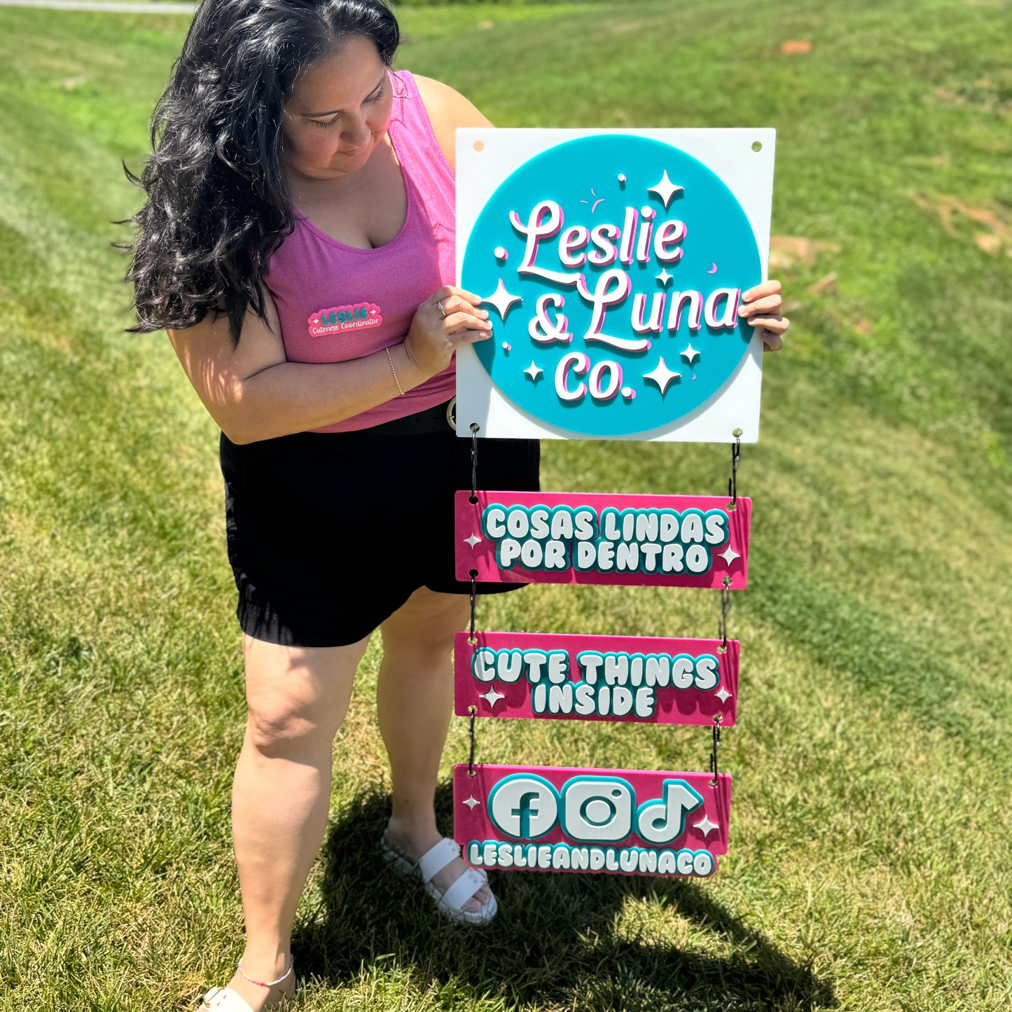 Woman holding a sign with 'Leslie & Luna Co.' branding in a grassy outdoor setting.