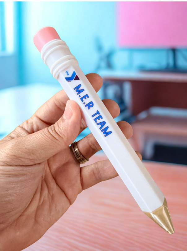 Hand holding a pen with 'YMER TEAM' branding in an indoor setting